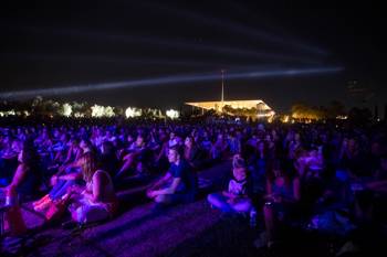 Crowds of people sit on the grass and picnic at night